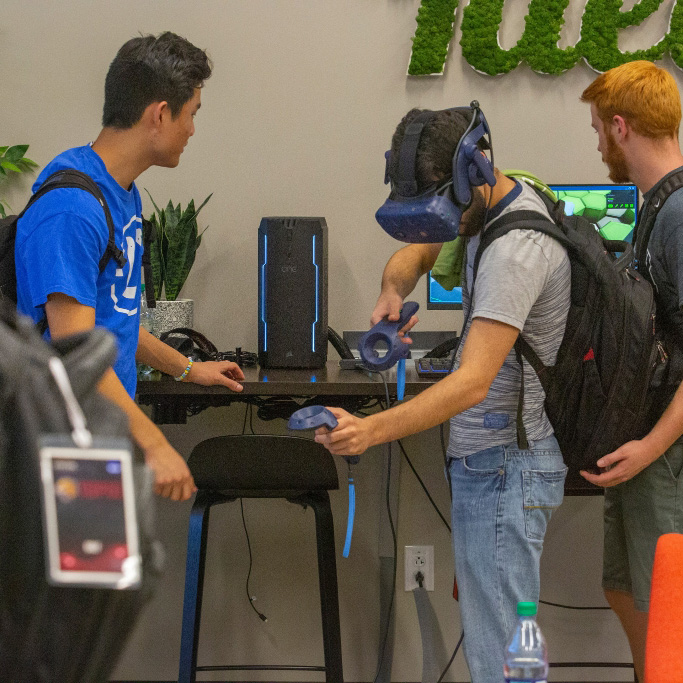 A student interacting with a VR headset while the other student watches him react to the experience
