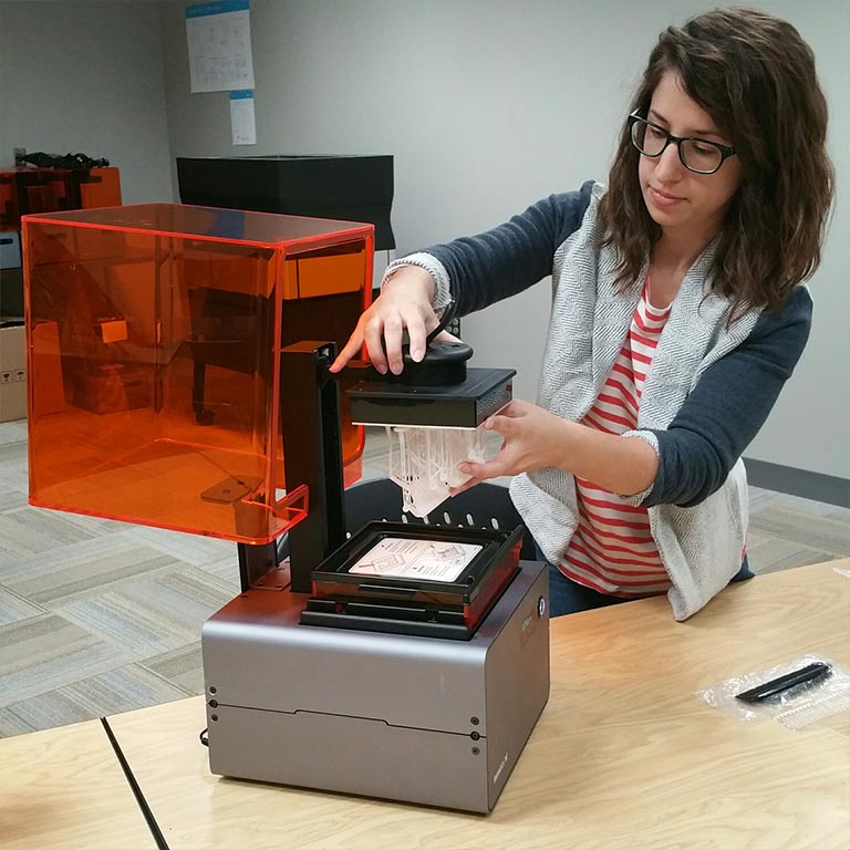A woman interacting with a 3D printer at the Think It Make It Lab